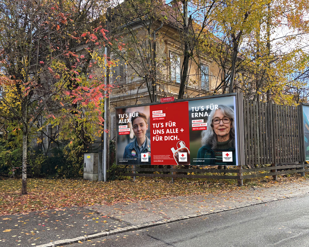 Große Plakatwand an einer Straße, umgeben von herbstlichen Bäumen. Links sieht man eine junge Person mit kurzem Haar und Jeansjacke. Text: „Tu’s für Alex. Sei dabei. Spende Blut. Rette Leben.“ In der Mitte ist ein rotes Plakat mit einem Blutbeutel und dem Text: „Tu’s für uns alle + für dich.“ Rechts sieht man eine ältere Frau mit grauen Haaren und Brille. Text: „Tu’s für Erna. Sei dabei. Spende Blut. Rette Leben.“ Alle Plakate tragen das Logo des Österreichischen Roten Kreuzes und die Website www.blut.at