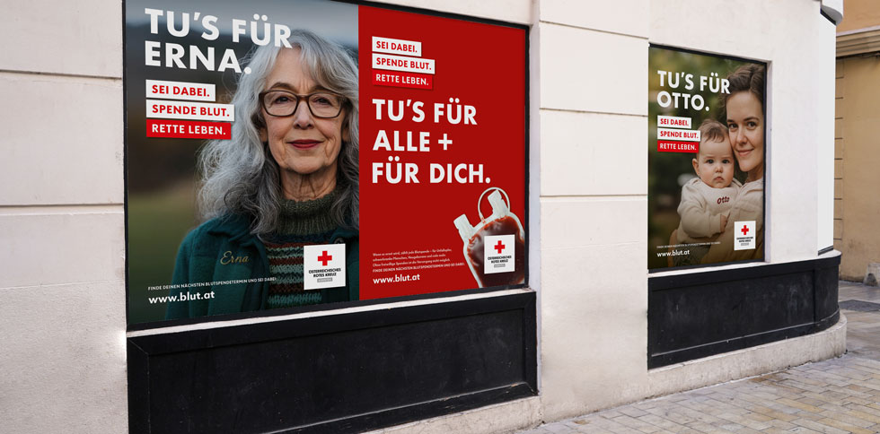 Großes Schaufenster mit drei Plakaten. Links sieht man eine ältere Frau mit grauen, langen Haaren und Brille. Text: „Tu’s für Erna. Sei dabei. Spende Blut. Rette Leben.“ In der Mitte ist ein rotes Plakat mit einem Blutbeutel und dem Text: „Tu’s für alle + für dich.“ Rechts sieht man eine junge Frau, die ein Baby im Arm hält. Text: „Tu’s für Otto. Sei dabei. Spende Blut. Rette Leben.“ Alle Plakate zeigen das Logo des Österreichischen Roten Kreuzes und die Website blut.at.